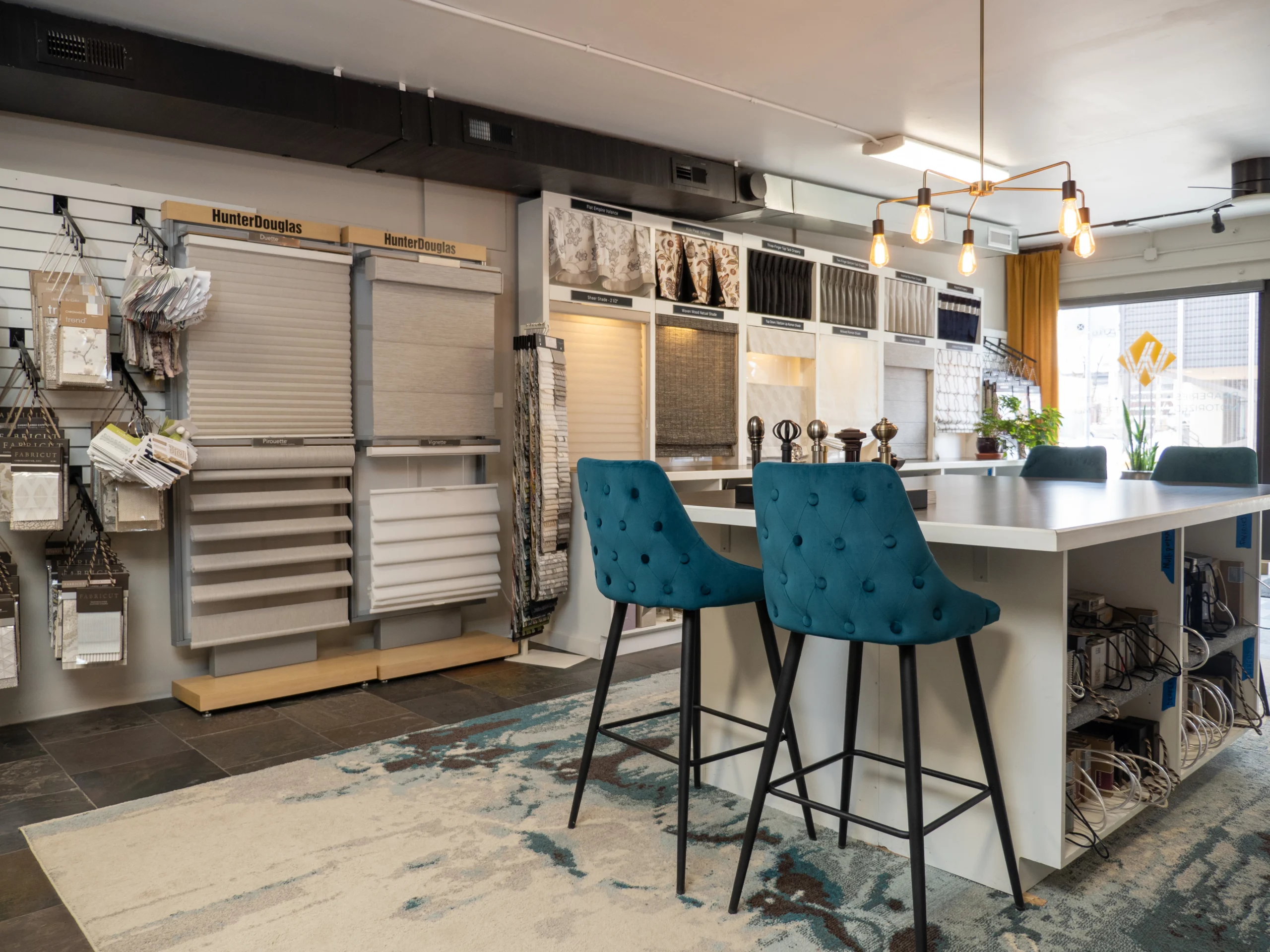 Modern interior design showroom in Denver with various fabric samples, stylish blue stools at a white counter, and elegant lighting fixtures.