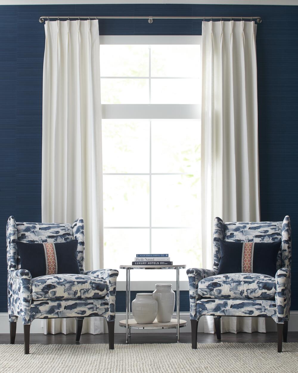 Two blue and white patterned armchairs flanking a small table with decorative items, set against a navy blue wall and a window draped with white curtains in Denver.